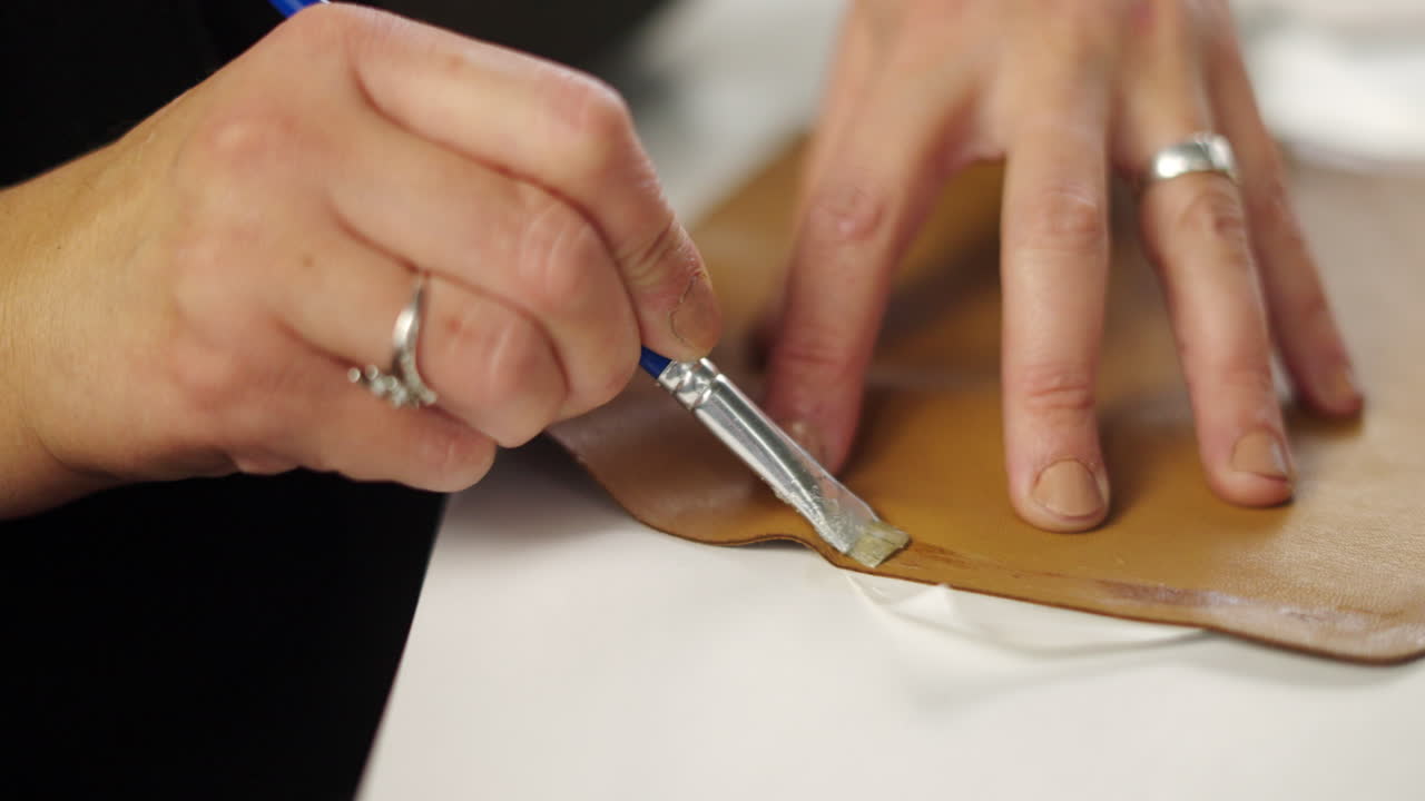 Close-up of hands painting leather with a brush