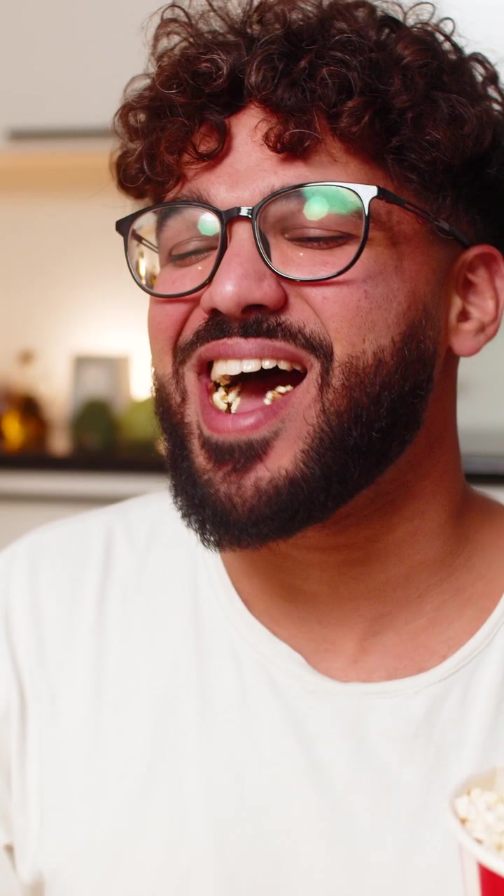 Arabian man eats popcorn watching movie film on laptop laughs reacts to scenes at night indoors