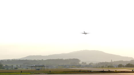 Plano-Amplio-Del-Despegue-Del-Avión-Durante-La-Puesta-De-Sol,-Fondo-De-Montaña