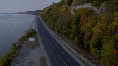 Aerial-descent-over-Great-River-Road-and-passing-cars-with-bluffs-and-River-in-Autumn