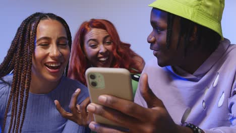 Close-Up-Studio-Shot-Of-Young-Gen-Z-Friends-Sitting-On-Sofa-Sharing-Social-Media-Post-On-Mobile-Phones-2