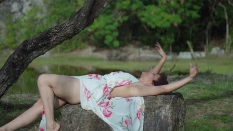 bonita latina de piel clara yace sobre una roca en el parque con un lago al fondo en un día soleado