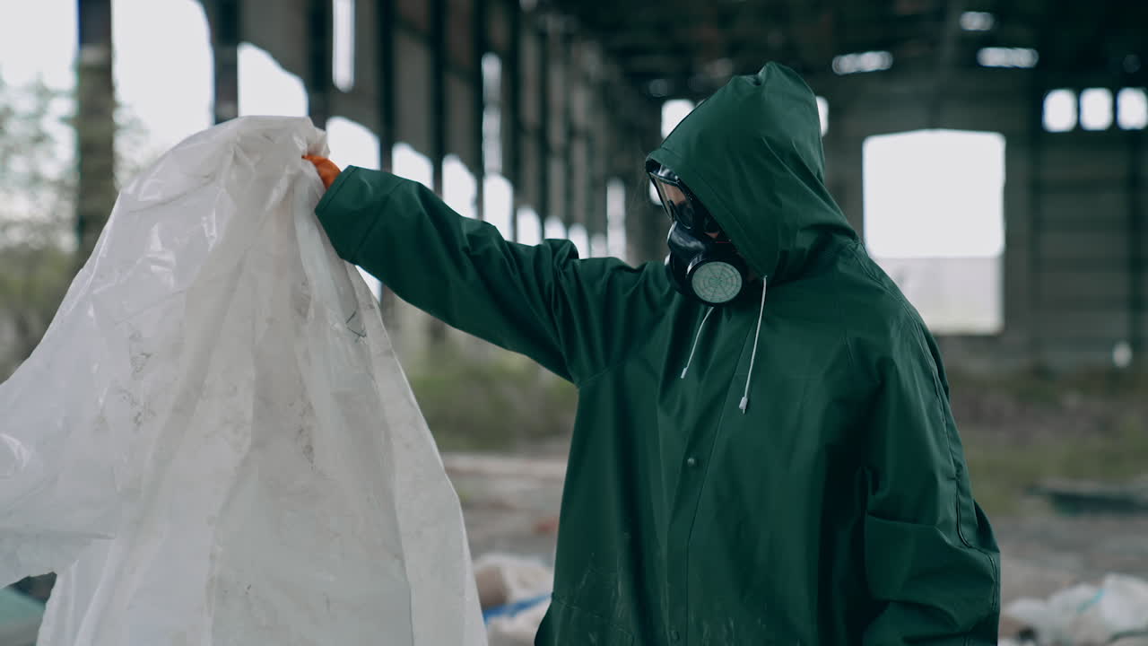 Scientist in abandoned place. Worker in protective suit and gas mask standing inside the ruined building with many garbage. Post-apocalyptic zone.