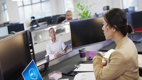 Asian-businesswoman-in-office-using-computer-with-video-call-and-ai-messaging-on-screens