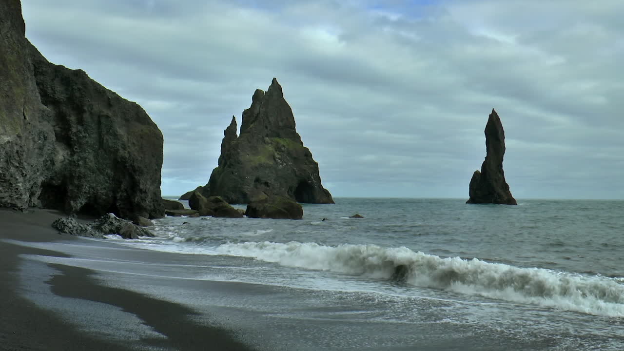 imágenes en cámara lenta de las olas del océano en la playa de arena negra reynisfjara con reynisdrangar - rocas marinas de basalto situadas bajo la montaña reynisfjall, cerca de la aldea de vik i myrdal en islandia