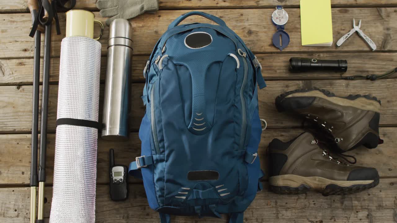 equipo de campamento con mochila, botas y termo sobre fondo de madera.