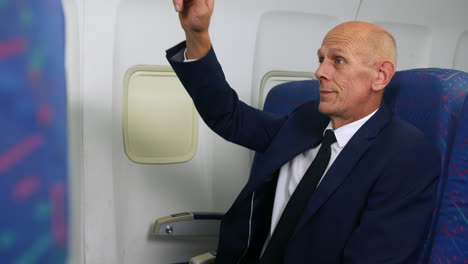 a mature businessman waving hand and calling for attention from the cabin crew on an airliner airplane