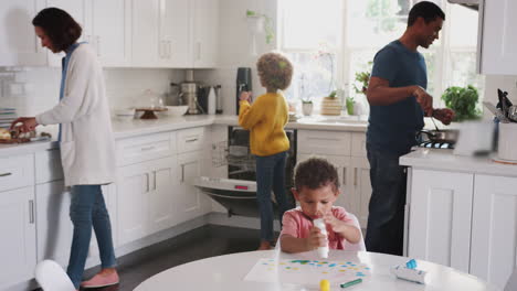 young african american boy painting a picture in kitchen while his family prepare food in the background
