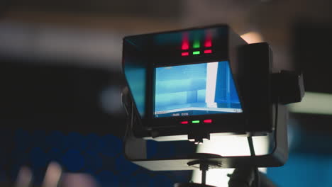 close-up view of camera monitor showing broadcast studio setup, red and green indicator lights on, and professional tv production environment. clear focus on blue-lit studio background