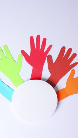 Vertical video of hands around circle made of colourful paper on white background with copy space