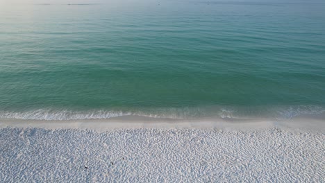 Aerial-view-of-waves-of-the-Gulf-of-Mexico-crashing-on-an-empty-white-sand-beach-in-Pensacola-Beach,-Florida-on-a-sunny-day-at-sunrise