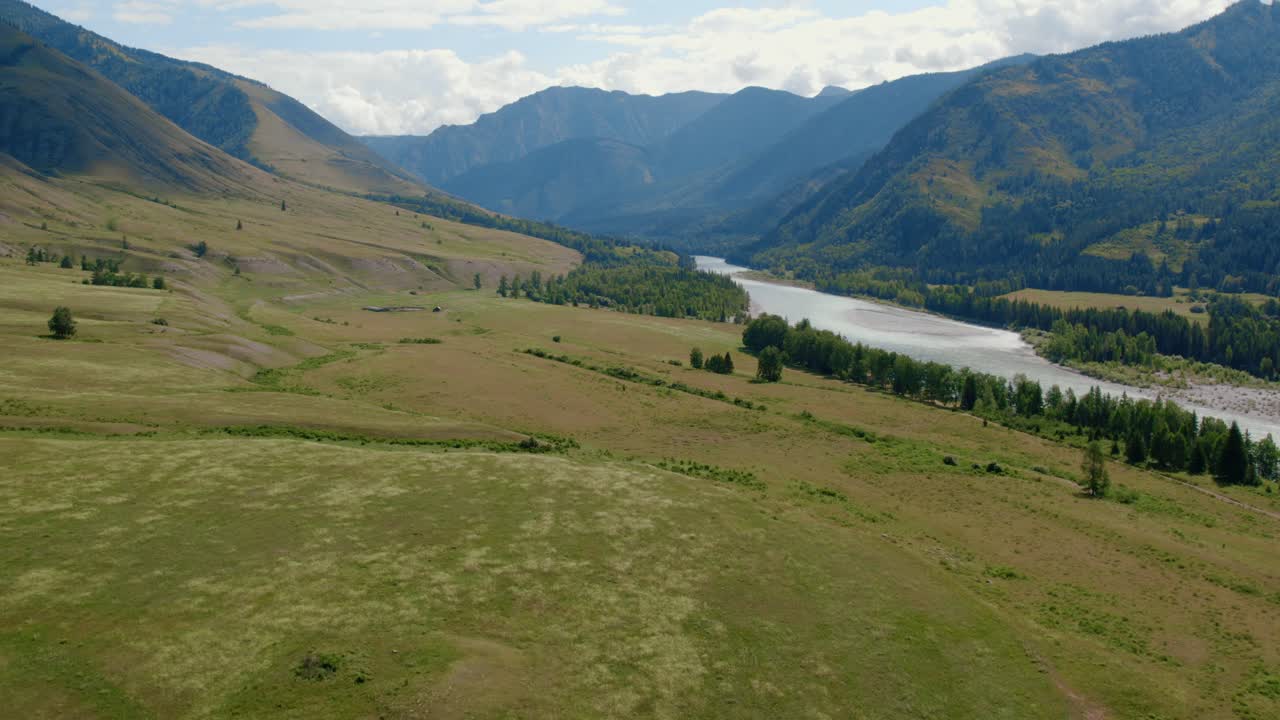 Ampie riprese aeree della Valle di Ak-Kem con un fiume tortuoso, prati verdi e pendii montuosi nella Repubblica dell'Altai, Russia, sotto un cielo estivo parzialmente nuvoloso