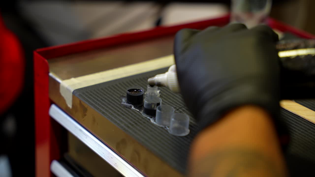 Tattoo artist hand with black glove carefully pouring drops of black ink into small cups before tattooing. Close up
