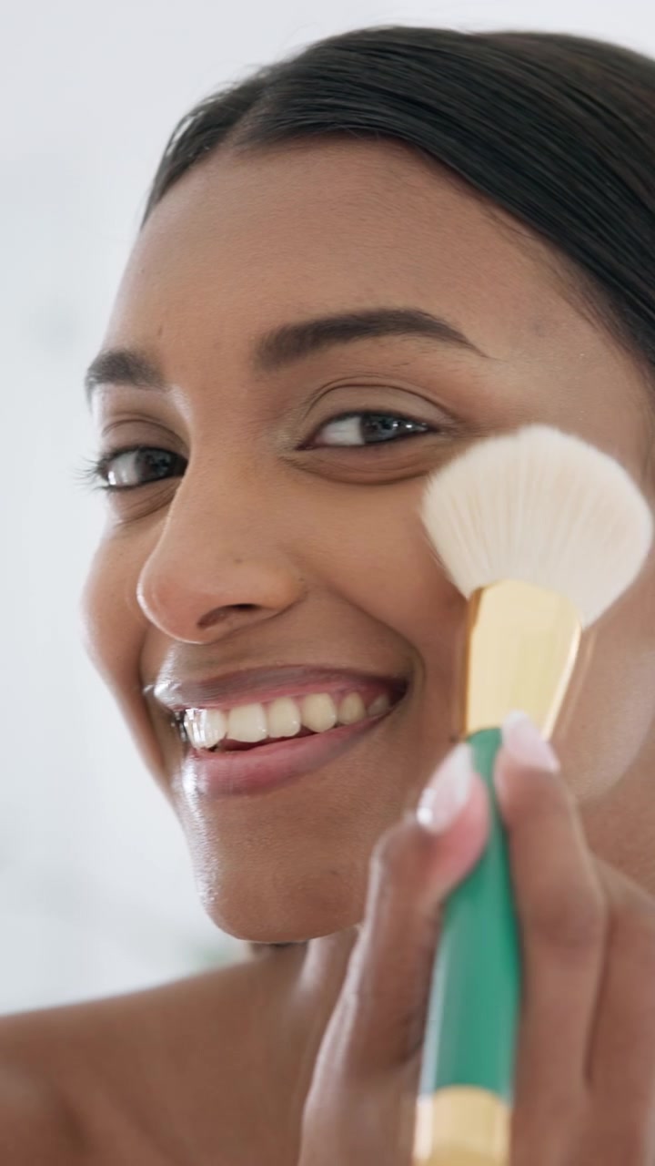 Young Woman Applying Makeup with Brush and Smiling at Camera