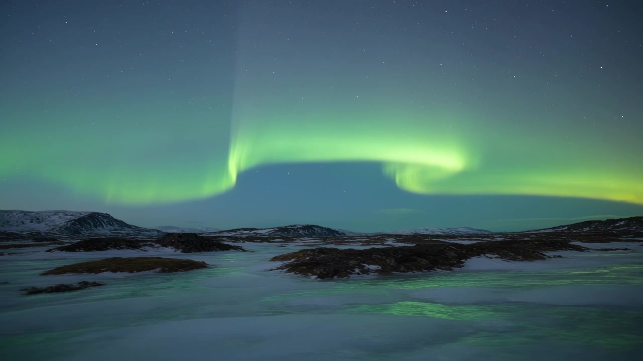 Skiftande grön norrskensbåge som reagerar på solvinden över en snöklädd slätt och förändrar isiga pölspeglingar.