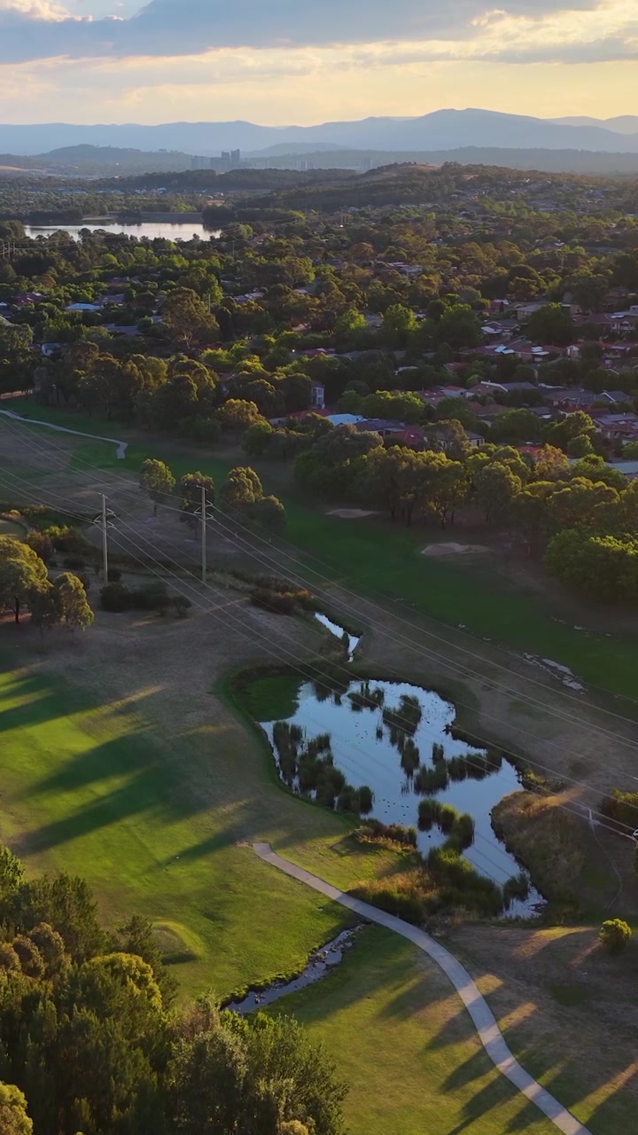 Ripresa con drone mostra un lussureggiante campo da golf e sobborghi residenziali durante un tramonto dorato.