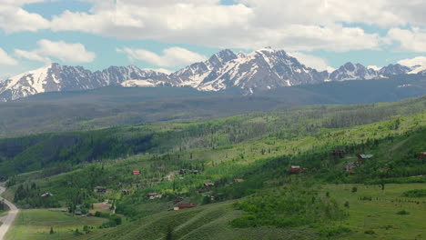 Closeup-aerial-view-of-beautiful-Colorado-mountain-range-with-snow-capped-peaks-on-a-sunny,-blue-sky-day-in-the-summer-with-green-fields,-trees,-and-mountain-homes