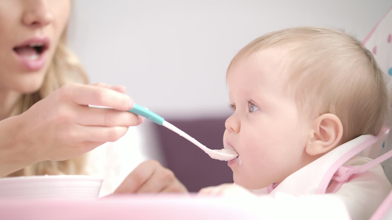 Baby eating puree with spoon. Mother feeding child with porridge