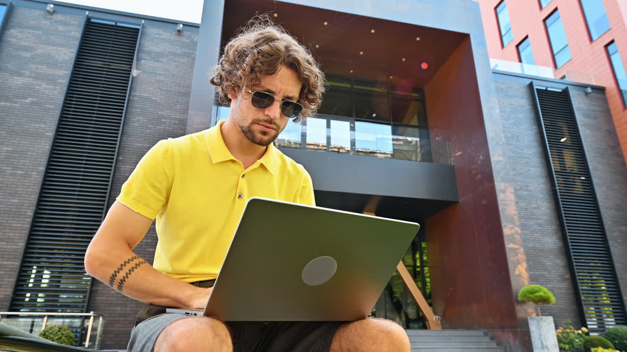 Man in yellow shirt talking standing on a bench and working on a laptop