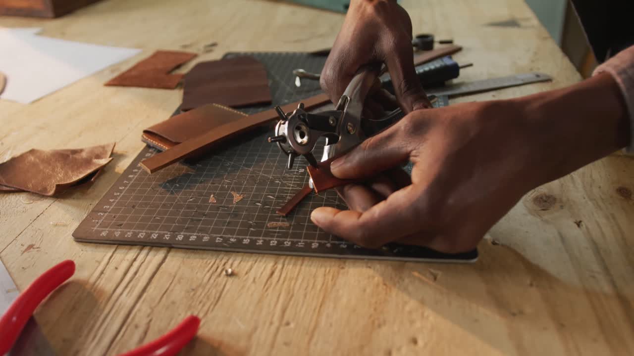 de manos artesano afroamericano usando herramientas para hacer un agujero en el taller de cuero