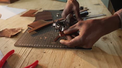 de manos artesano afroamericano usando herramientas para hacer un agujero en el taller de cuero