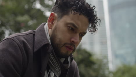 a sad, depressed and worried businessman sitting on a bench in a park alone, stare into the ground, submerged in thoughts