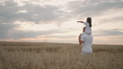 papá lleva en sus hombros a su amada hija sana en el sol. en cámara lenta la hija camina con su padre por el campo y libre y feliz levanta las manos. caminando por el campo.