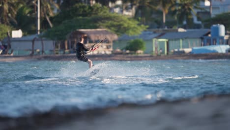 Rückansicht-Eines-Kiteboarders,-Der-Hüpft-Und-Springt,-Während-Er-Sich-Erhebt,-Um-Eine-360-Grad-Drehung-Zu-Machen,-Unscharfer-Hintergrund-Des-Hauses-Und-Der-Küste-Der-Dominikanischen-Republik