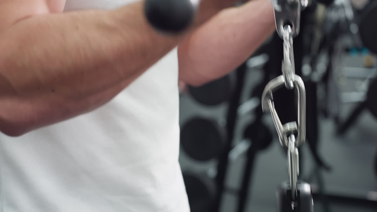 Male hand wearing wrist watch grips cable machine bar and pulls weight in gym setting, veins and muscles visible, demonstrating strength training motion under focused fitness environment lighting