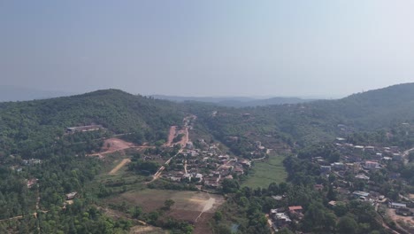 the aerial view showcases a picturesque rural village nestled amidst a sprawling landscape of lush green hills. the camera glides over the scene, revealing a cluster of houses with red-tiled