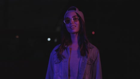 teenager caucasian girl with glasses and cap smiling and looking at camera outdoors at night