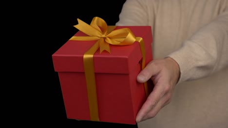 red gift box in hands of adult caucasian man in beige sweater. close up locked shot. celebration eve. event christmas new year thanksgiving day black friday birthday mothers fathers valentines day.