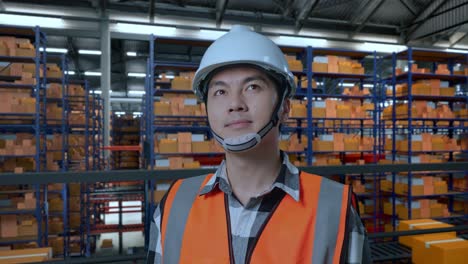 primer plano de un ingeniero asiático con casco de seguridad de pie en el almacén con estantes llenos de mercancías de entrega. mirando a su alrededor, comprobando el stock en los estantes