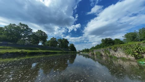 Zeitraffer-Eines-Ruhigen-Wasserwegs-Mit-üppigem-Grün-Unter-Einem-Weiten-Himmel-Mit-Vereinzelten-Wolken