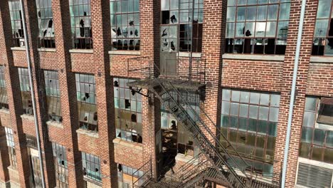 abandoned brick building with fire escape and large shattered windows