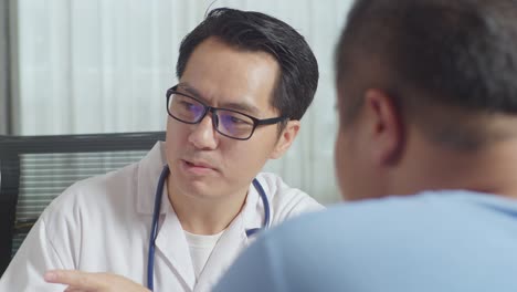 close up of asian male doctor with a fat male patient in clinic, sitting at desk and discussing about the results of medical check up on a tablet