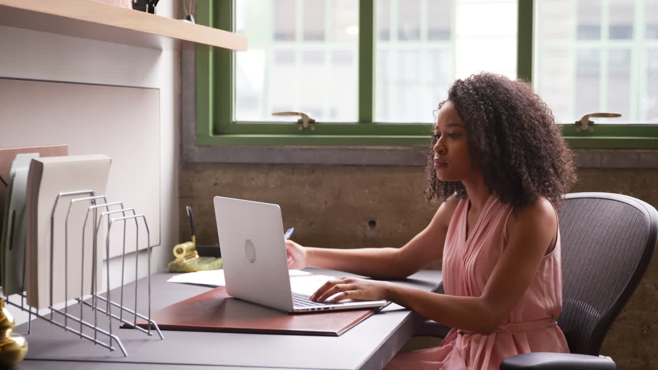 Young black woman working alone with laptop in small office
