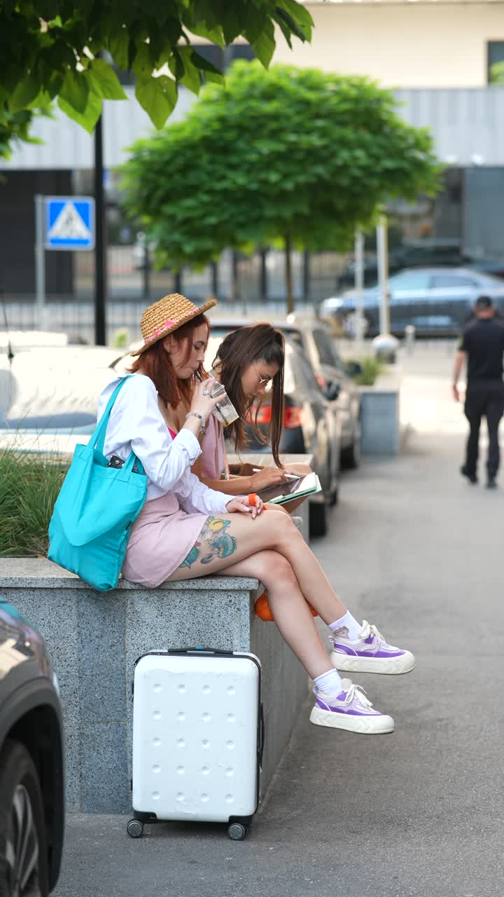 dos mujeres sentadas en la calle, disfrutando de una copa y mirando un mapa.