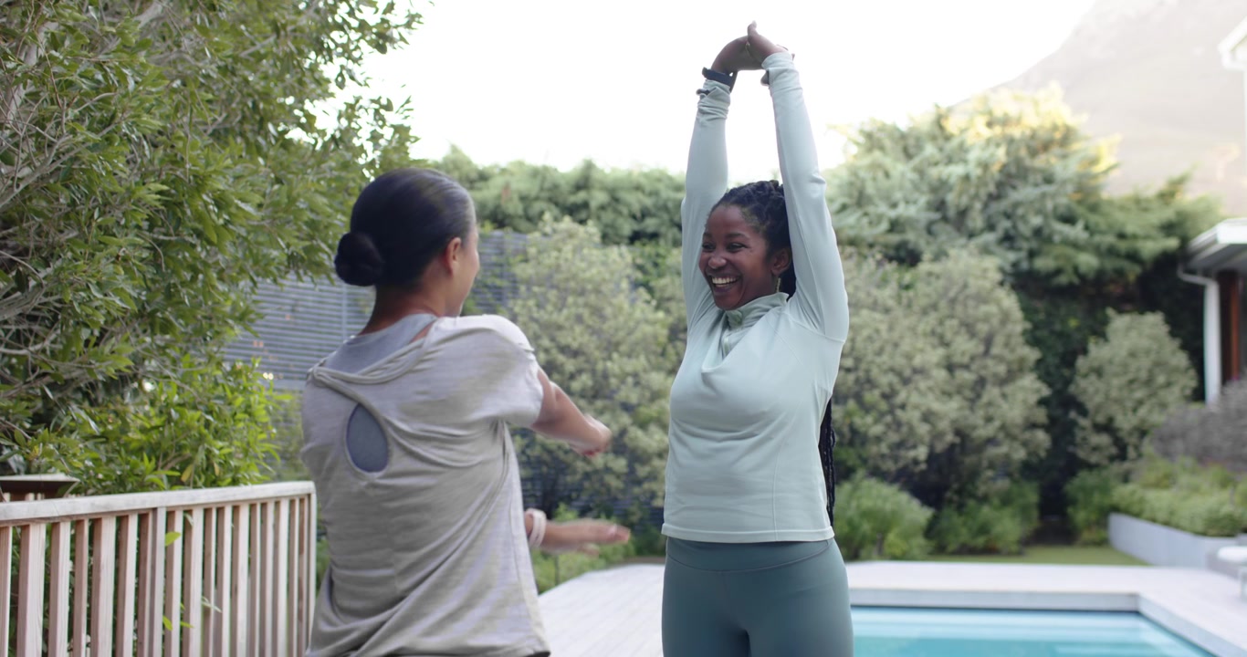Amiche afroamericane si riscaldano in abiti da allenamento, la donna a destra fa da guida sul bordo piscina