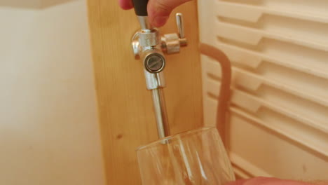 pouring beer with bubbles and foam in glass from tap with hand holding it