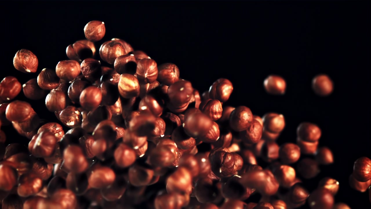 Nocciole che cadono e scompaiono al rallentatore su sfondo nero