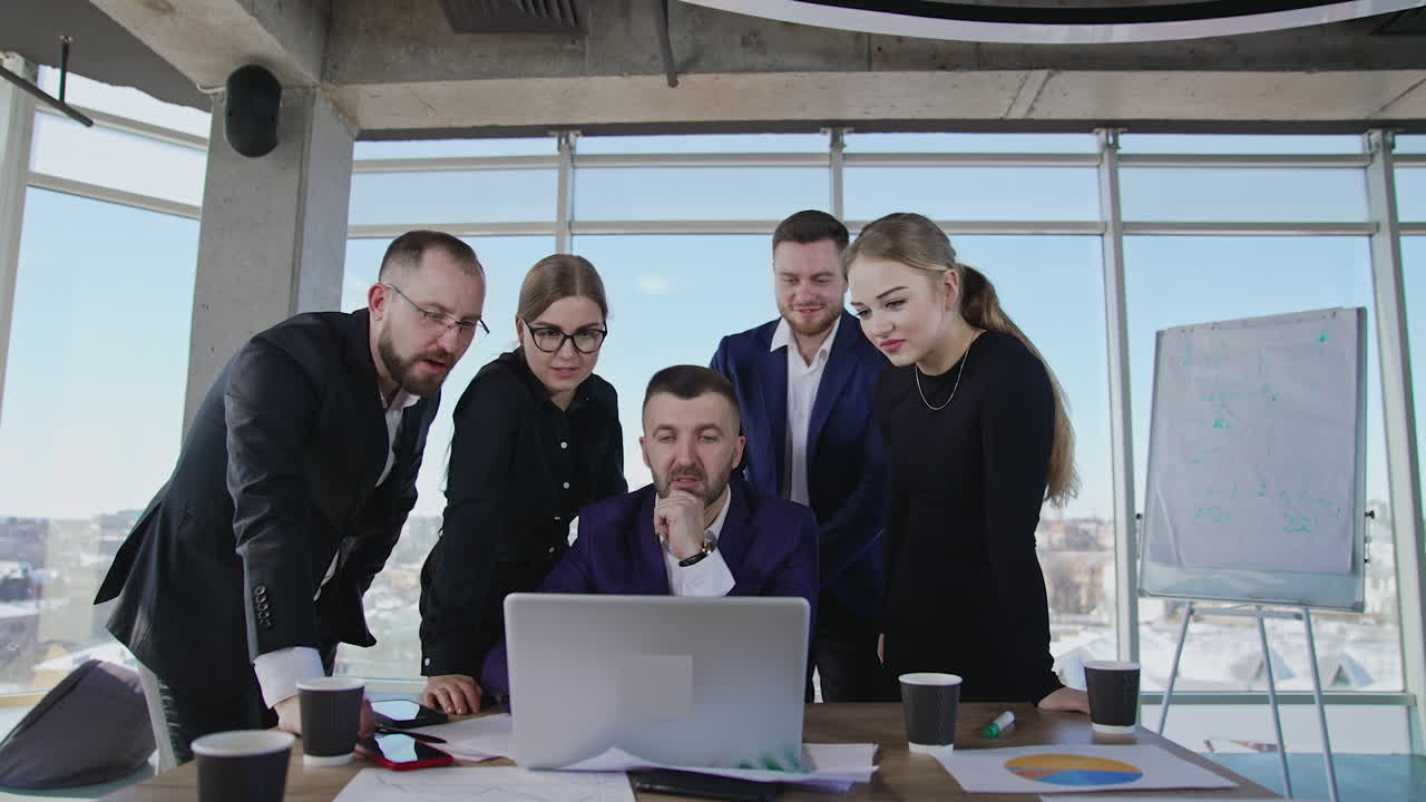 Teammates standing around the boss who's sitting in front of laptop. Brainstorming group collaborate and discuss something in computer.
