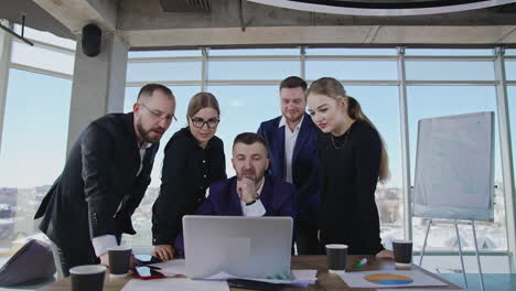 teammates standing around the boss who's sitting in front of laptop. brainstorming group collaborate and discuss something in computer.