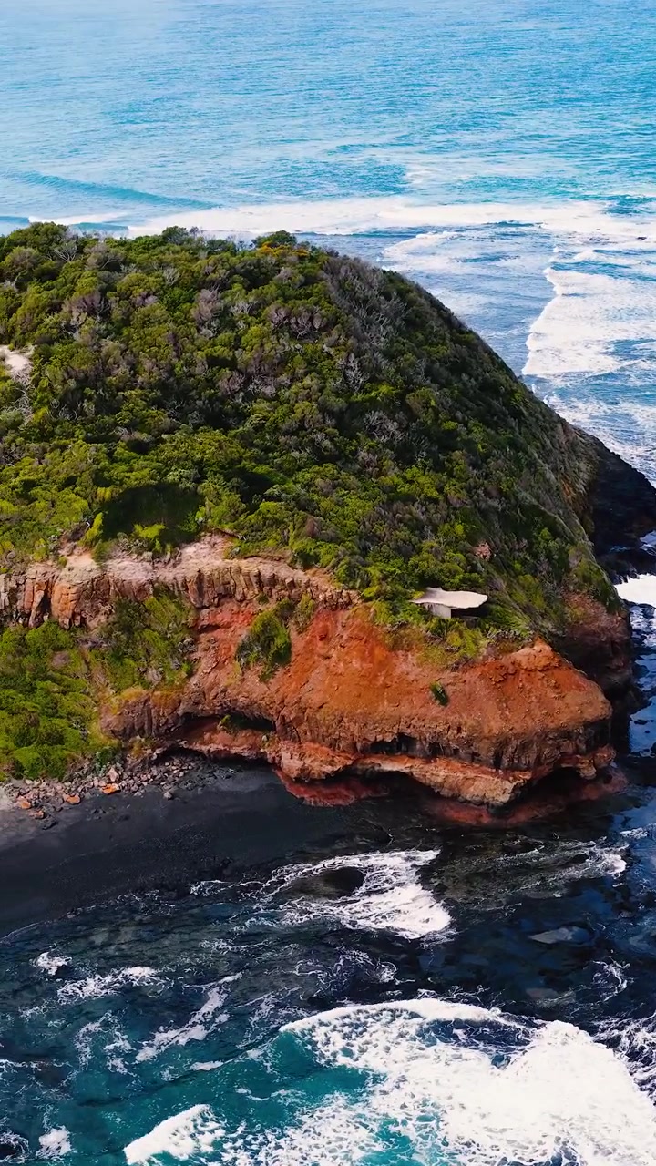 Vista aerea inclinata dalle onde turchesi dell'oceano alle lussureggianti scogliere costiere verdi a Flinders, Australia