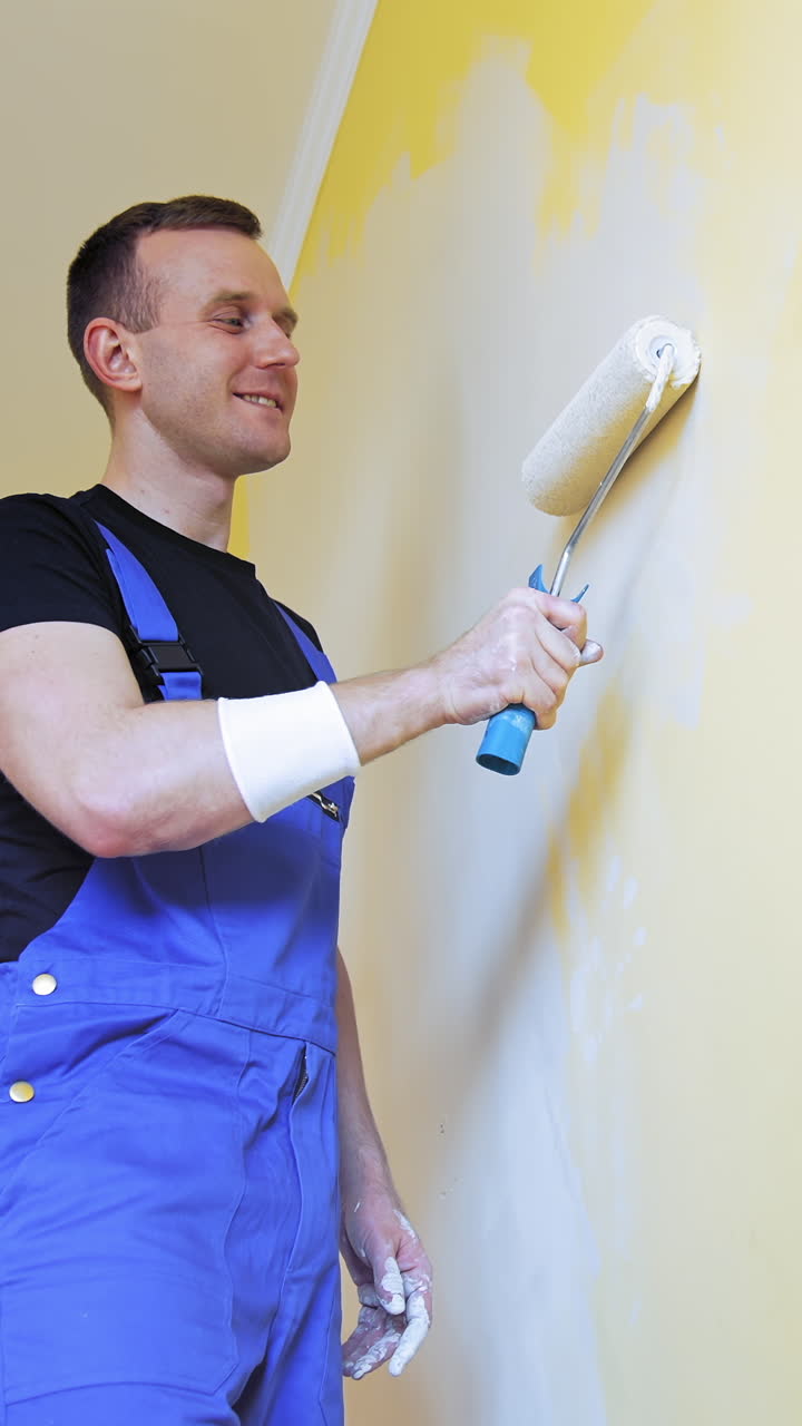 Man painting walls at home. Handsome man in work overalls paints the wall with a roller