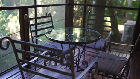 cozy hotel room balcony featuring elegant iron furniture, including a round glass table and four chairs, overlooks lush greenery, providing a serene and inviting outdoor space