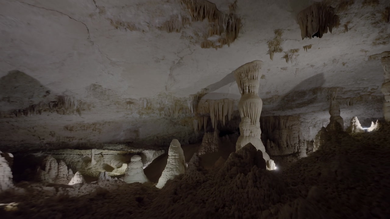 Dimly Lit Limestone Cave Interior Showcasing Towering Stalagmites And Stalactites Surrounding Massive Column