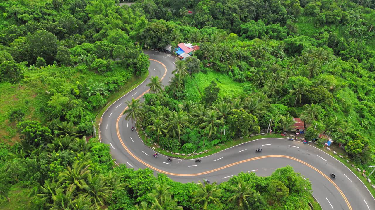 The camera surveys a winding road from above, revealing a route embraced by vibrant vegetation and occasional structures, near Mauban, Quezon