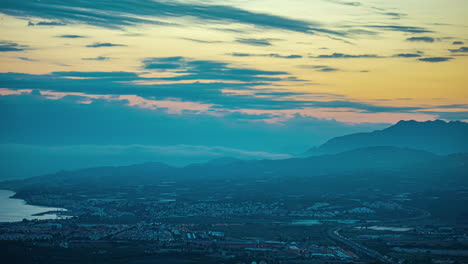 Orange-golden-hour-sky-recedes-to-dusk-glow-as-Malaga-Spain-city-lights-up-at-night