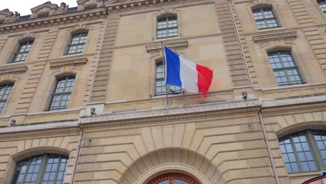 bandera nacional ondeando frente a un edificio arquitectónico en parís, francia